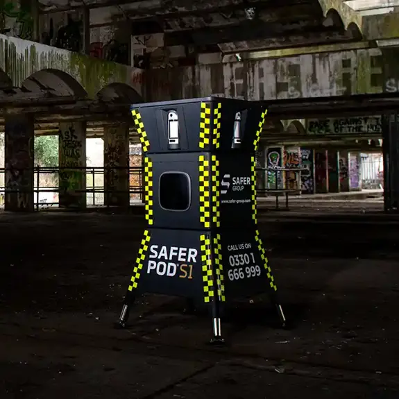 A yellow and black safer POD s1 device stands inside an abandoned, dilapidated building with graffiti and overgrown foliage visible outside.