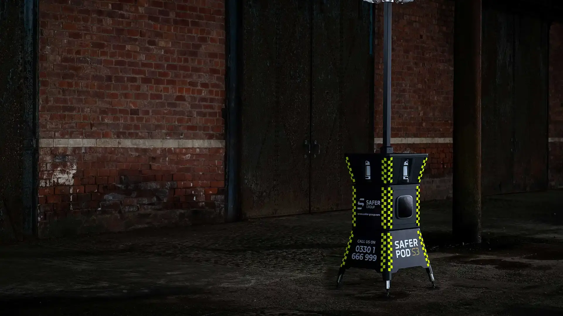 A Safer Pod S3 security unit stands in a dimly lit, industrial space against a brick wall.