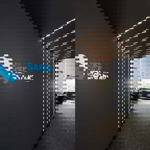 A sleek office hallway featuring a "Safer Scotland" logo on the wall, with modern lighting and glass-panelled meeting rooms.