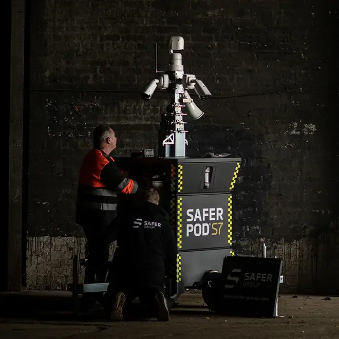 Two men working on the side panel of a Safer POD S7 security device.