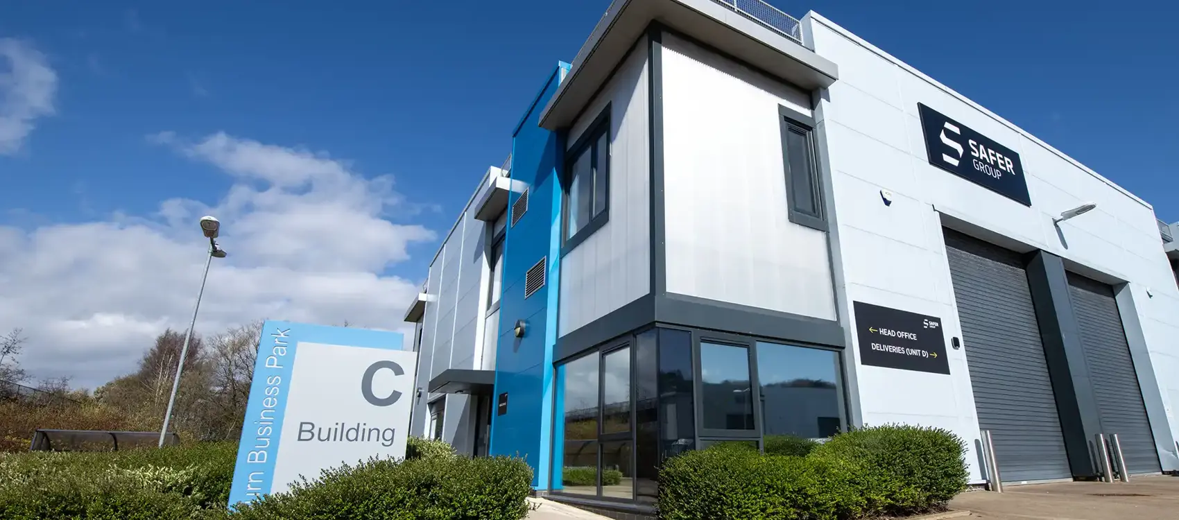 Modern business building with a blue accent, clear signage for "Building C," and a sunny sky in the background.