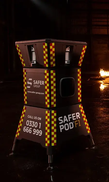 Two black safer pod F1s with yellow and red reflective patterns stand in a dimly lit space, flames flicker in the background alongside a Safer POD F7.