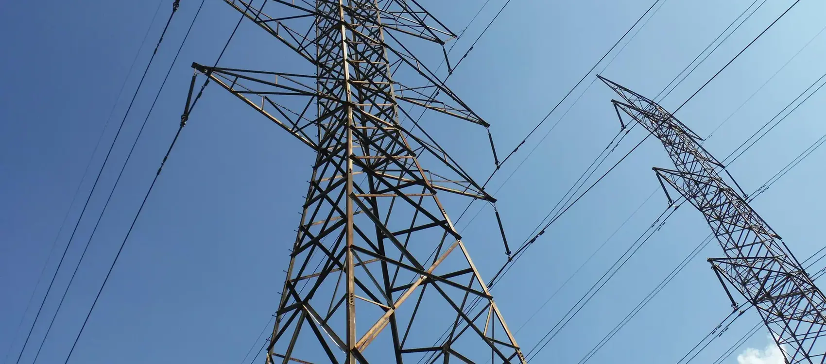 Two towering power transmission lines stretch against a bright blue sky, showcasing their metal structures and connecting wires.