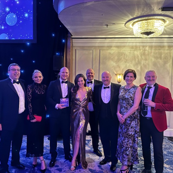 A group of elegantly dressed individuals posing together at a glamorous event, with soft lighting and a starry backdrop.