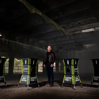 A dimly lit, abandoned building features four Safer Pod S1 devices, with Group chief executive Ryan Clark standing in the middle of them.