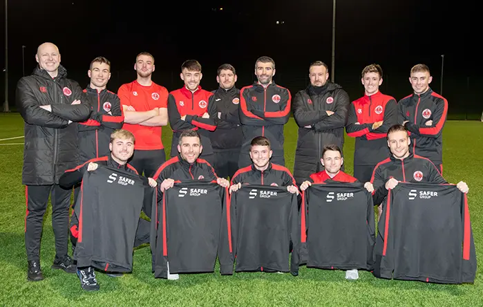 Greenock Juniours football team, on a football pitch holding Safer Group branded shirts.