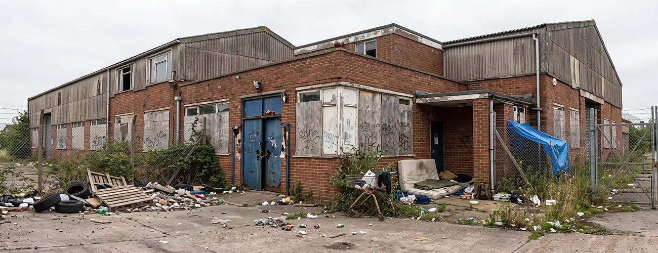 Exterior of a vacant property, covered in graffiti and surrounded by litter