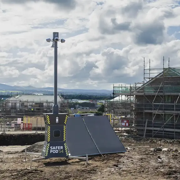 A Safer Pod S4 security device, with two solar panels beside it, is on a construction site with scaffolding and cloudy sky in the background enhancing site safety and security.