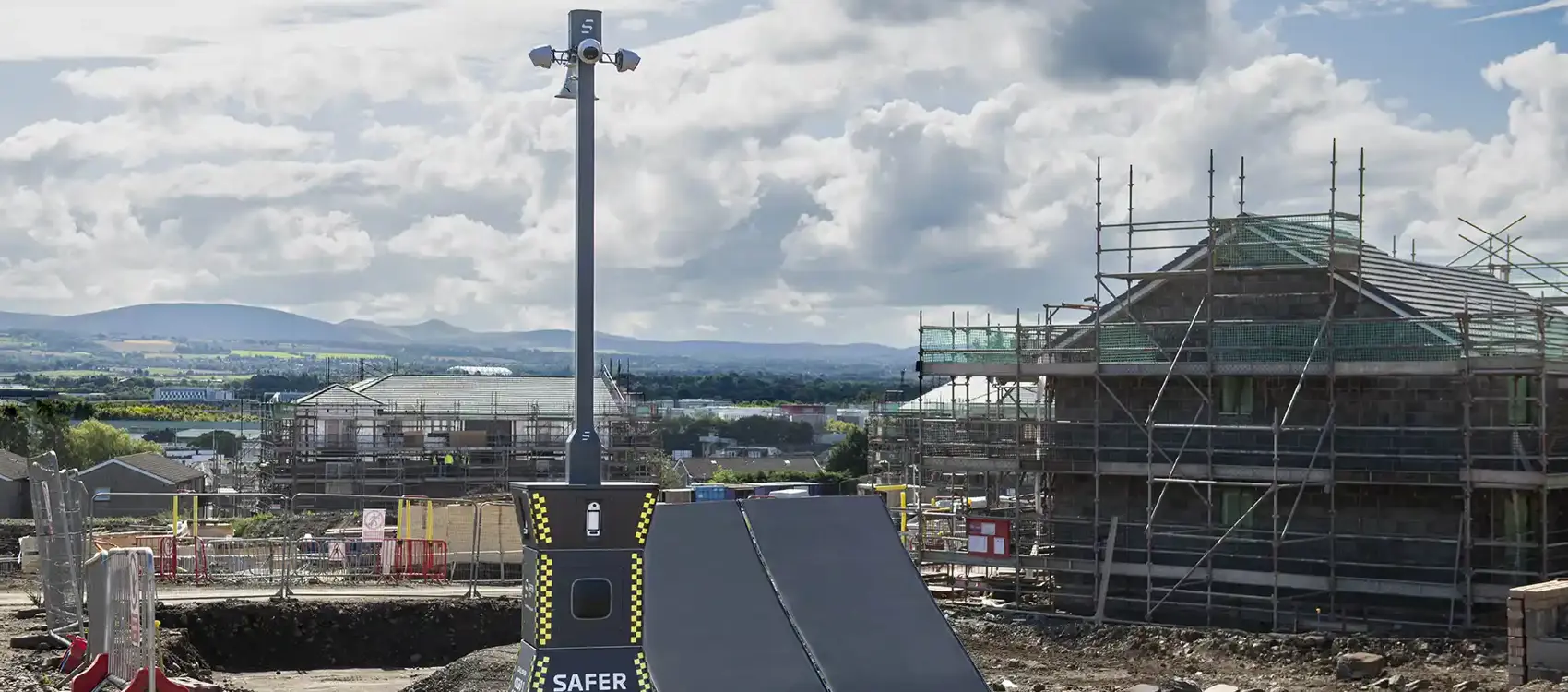 A Safer Pod S4 security device, with two solar panels beside it, is on a construction site with scaffolding and cloudy sky in the background enhancing site safety and security.