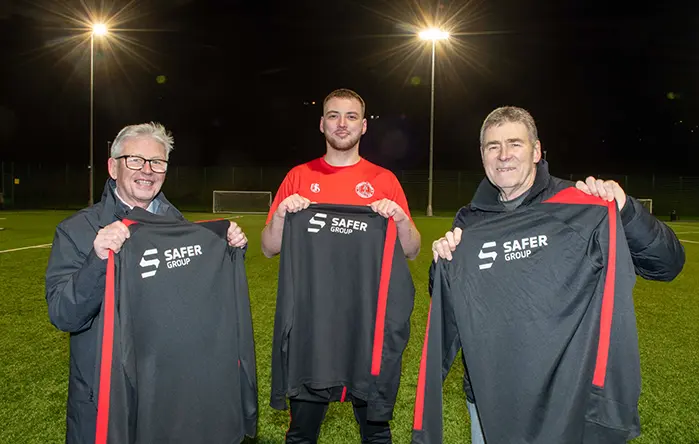 Members of the Greenock Juniors football team holding Safer Group branded shirts.