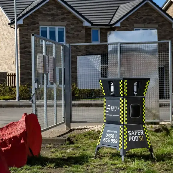 A Safer Group S1 pod in front of newly built homes, surrounded by a fenced construction site and red boulders.