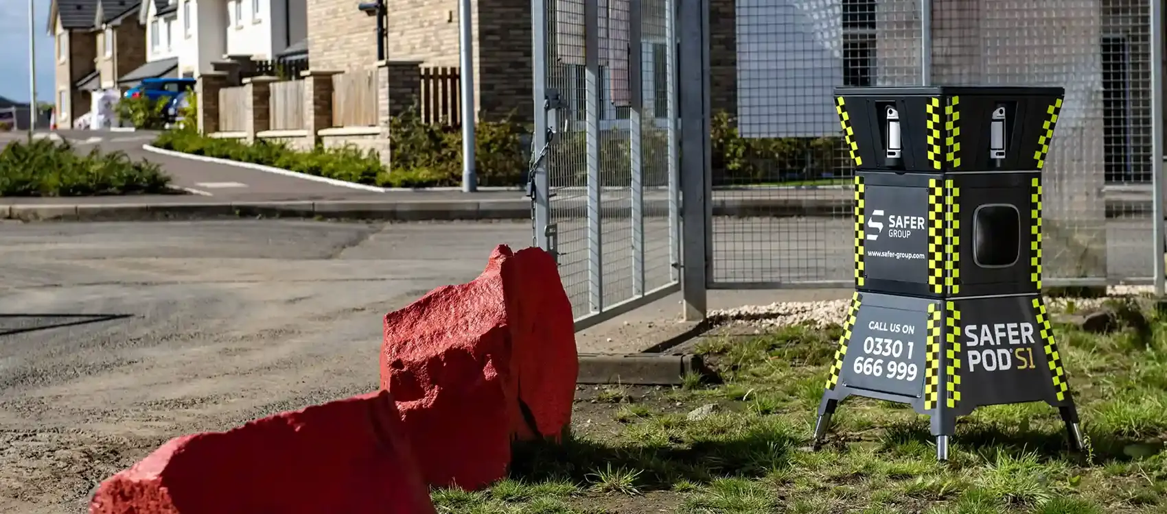 A Safer Group S1 pod in front of newly built homes, surrounded by a fenced construction site and red boulders.